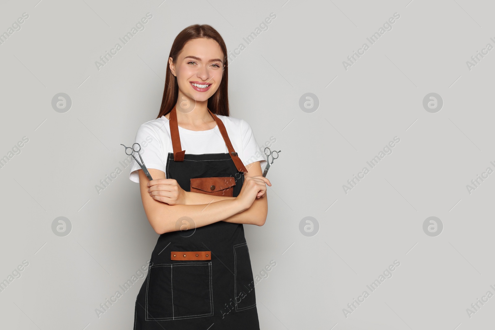 Photo of Portrait of happy hairdresser with professional scissors on light background. Space for text