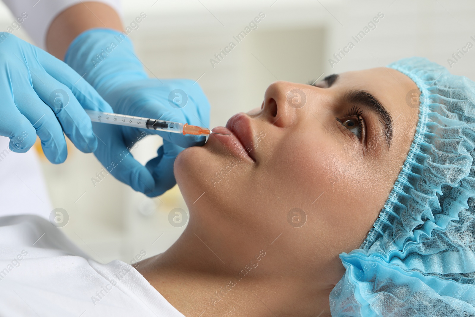 Photo of Doctor giving lips injection to young woman in clinic, closeup. Cosmetic surgery