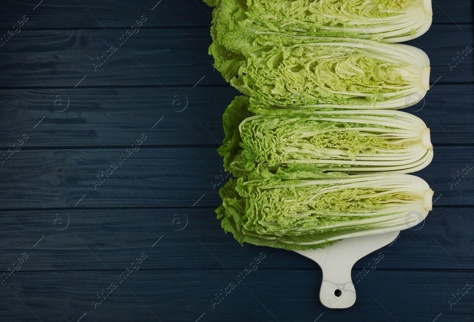 Photo of Cut fresh ripe Chinese cabbages on blue wooden table, flat lay. Space for text