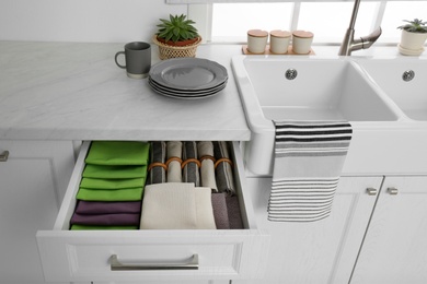 Photo of Open drawer with different folded towels and napkins in kitchen