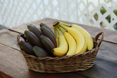 Photo of Wicker basket with tasty purple and yellow bananas on wooden table