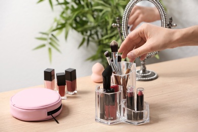 Woman taking cosmetic products for makeup from organizer on dressing table, closeup. Space for text