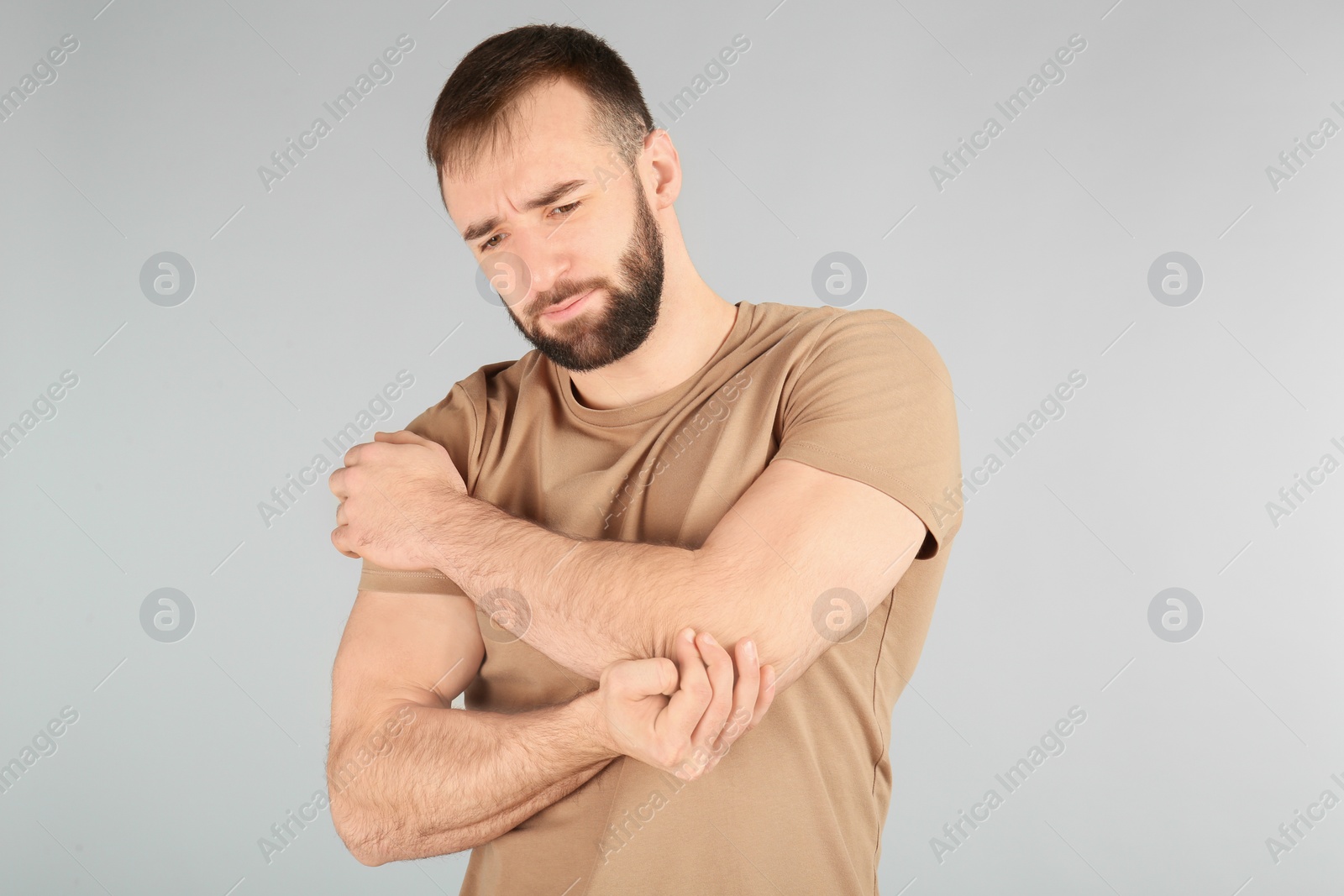 Photo of Young man suffering from pain in elbow on light background