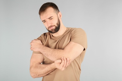 Young man suffering from pain in elbow on light background