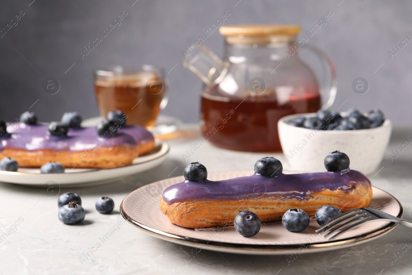 Photo of Tasty glazed eclairs with blueberries on grey marble table, closeup