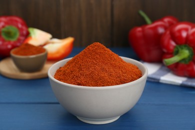 Bowl with aromatic paprika powder and fresh bell peppers on blue wooden table