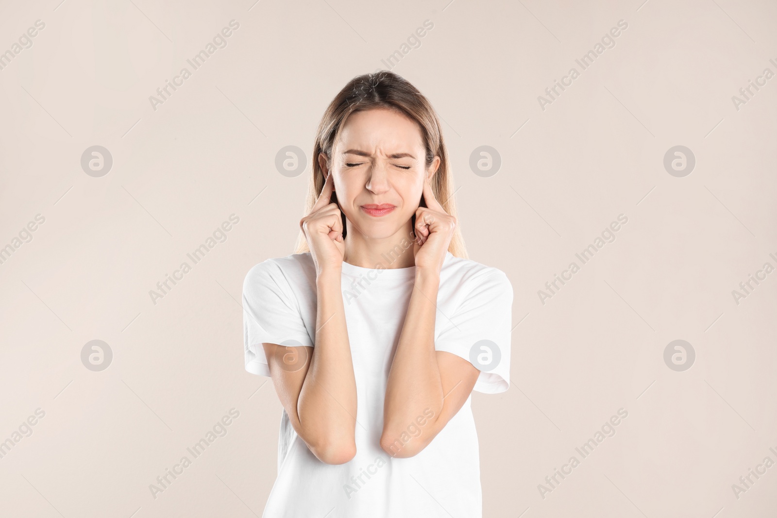 Photo of Emotional young woman covering her ears with fingers on beige background