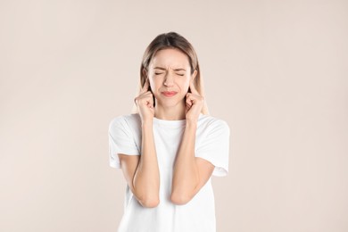 Photo of Emotional young woman covering her ears with fingers on beige background