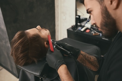 Hairdresser trimming client's beard in barbershop. Professional shaving service