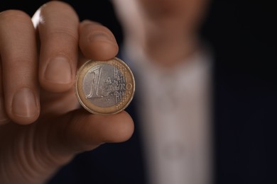 Woman holding 1 euro coin on black background, closeup