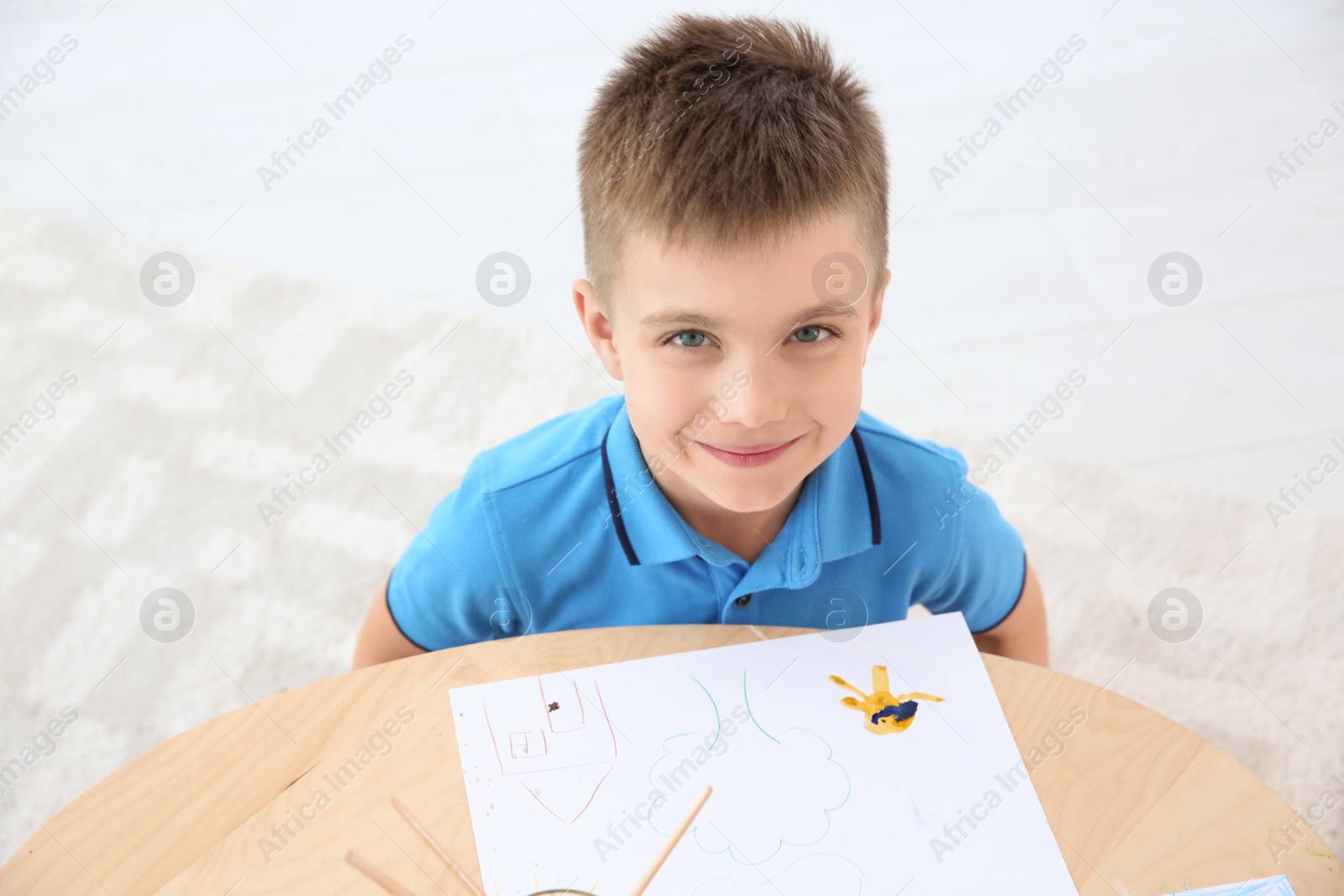 Photo of Cute little child painting at table, indoors. Playing room