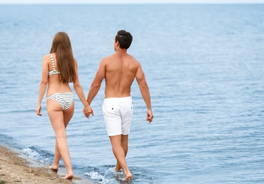 Happy young couple walking together on sea beach. Space for text