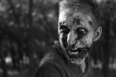 Photo of Scary zombie outdoors, black and white effect. Halloween monster