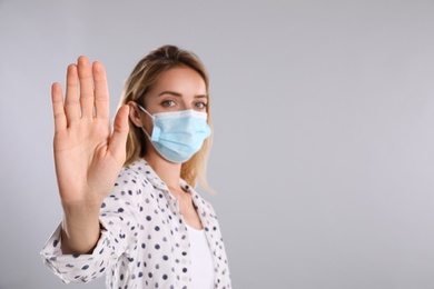 Photo of Woman in protective face mask showing stop gesture on grey background, focus on hand. Prevent spreading of coronavirus