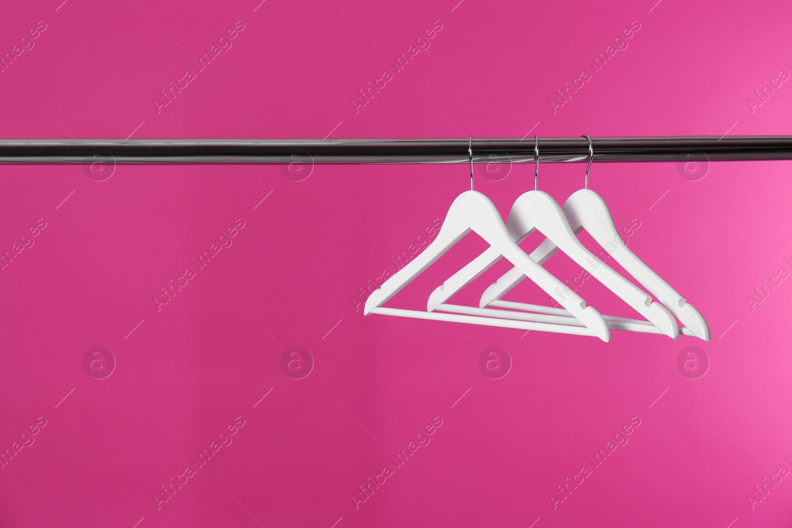 Photo of Metal rack with clothes hangers on color background, space for text