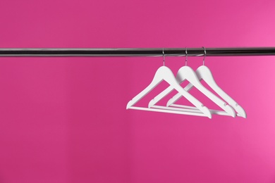 Photo of Metal rack with clothes hangers on color background, space for text