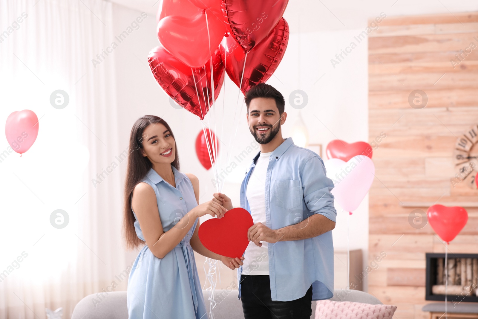 Photo of Lovely couple with heart shaped balloons in living room. Valentine's day celebration