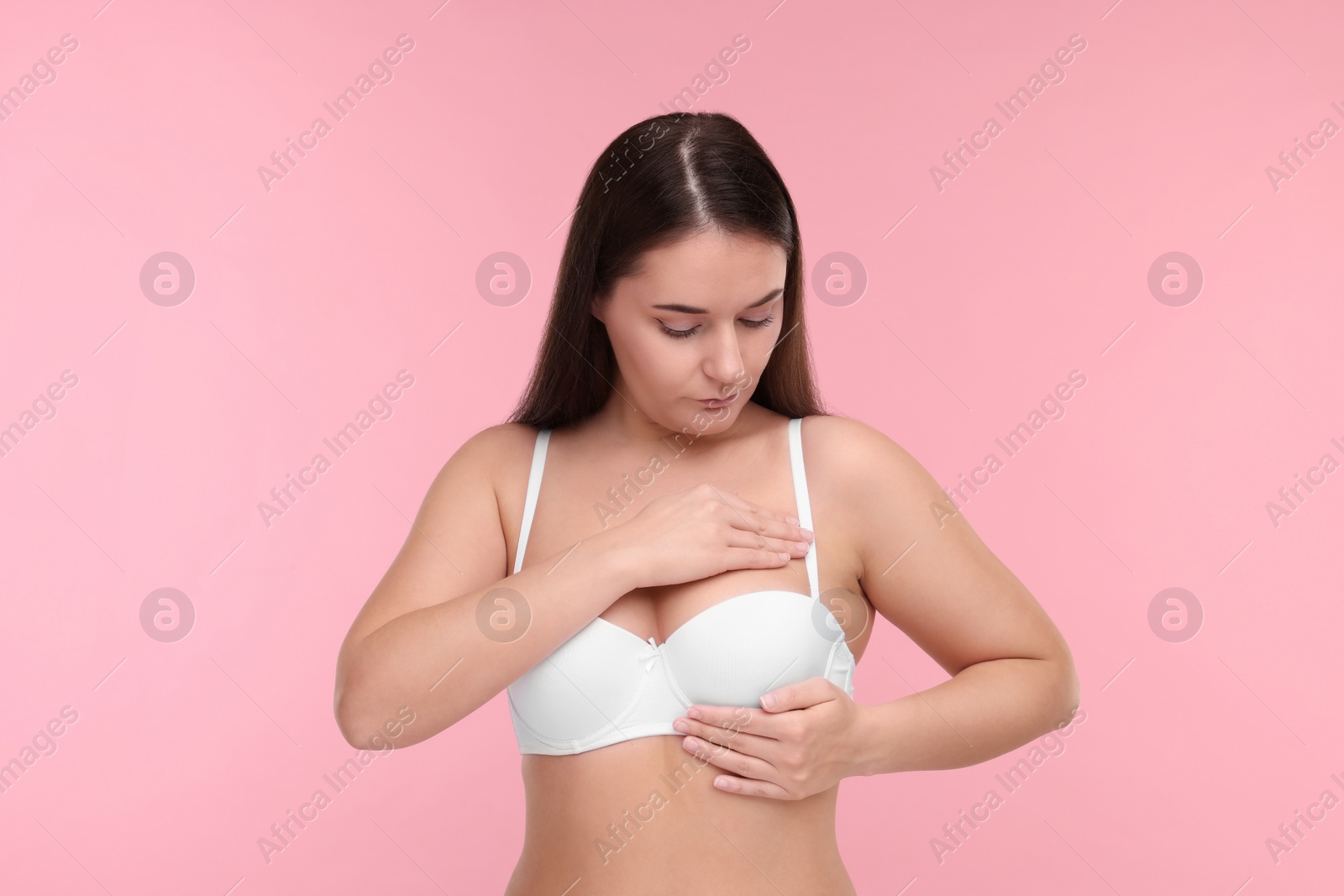 Photo of Mammology. Woman in bra doing breast self-examination on pink background