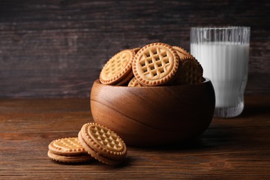 Photo of Tasty sandwich cookies with cream and glass of milk on wooden table