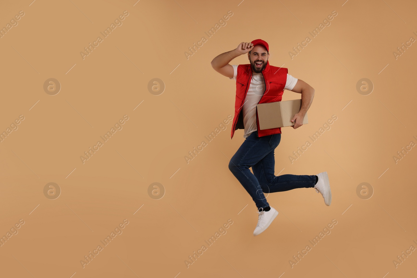 Photo of Happy young courier jumping with parcel on light brown background, space for text