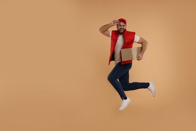 Happy young courier jumping with parcel on light brown background, space for text