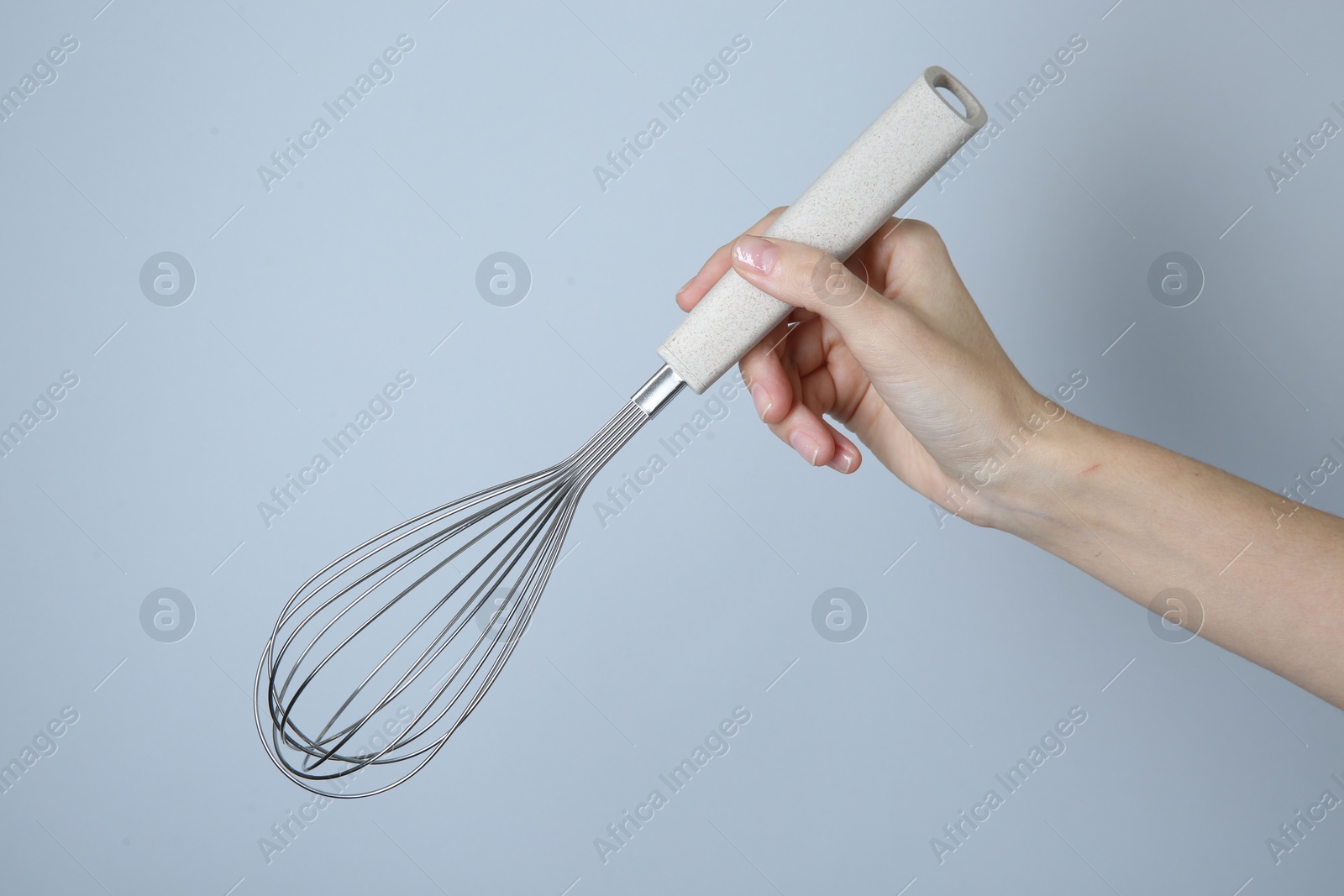 Photo of Woman holding metal whisk on light grey background, closeup