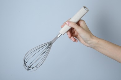 Woman holding metal whisk on light grey background, closeup