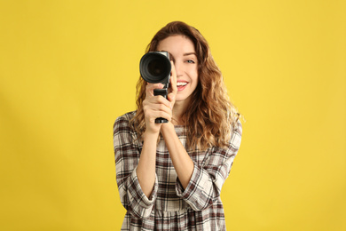 Beautiful young woman with vintage video camera on yellow background