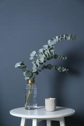 Photo of Beautiful eucalyptus branches and burning candle on white table near blue wall. Interior element