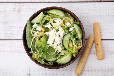 Bowl of tasty salad with leek, cheese and grissini on white wooden table, top view