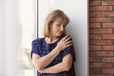 Photo of Senior woman suffering from depression near window