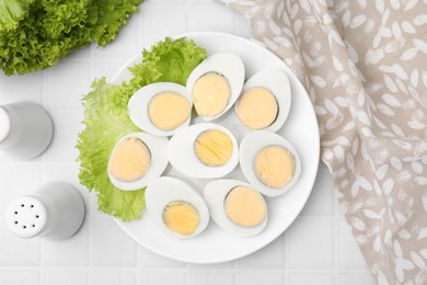 Photo of Fresh hard boiled eggs and lettuce on white tiled table, flat lay