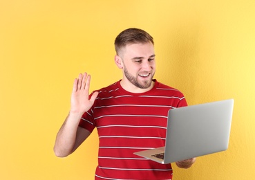 Young man using video chat on laptop against color background