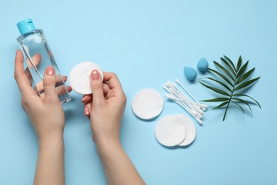 Woman with makeup remover, sponges, cotton pads and buds on light blue background, top view