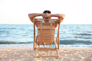 Young man relaxing in deck chair on beach near sea