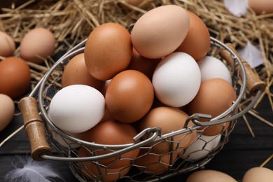 Fresh chicken eggs and dried straw on black wooden table, closeup