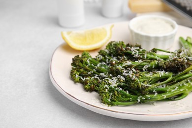 Tasty cooked broccolini with cheese, lemon and sauce on light table, closeup. Space for text