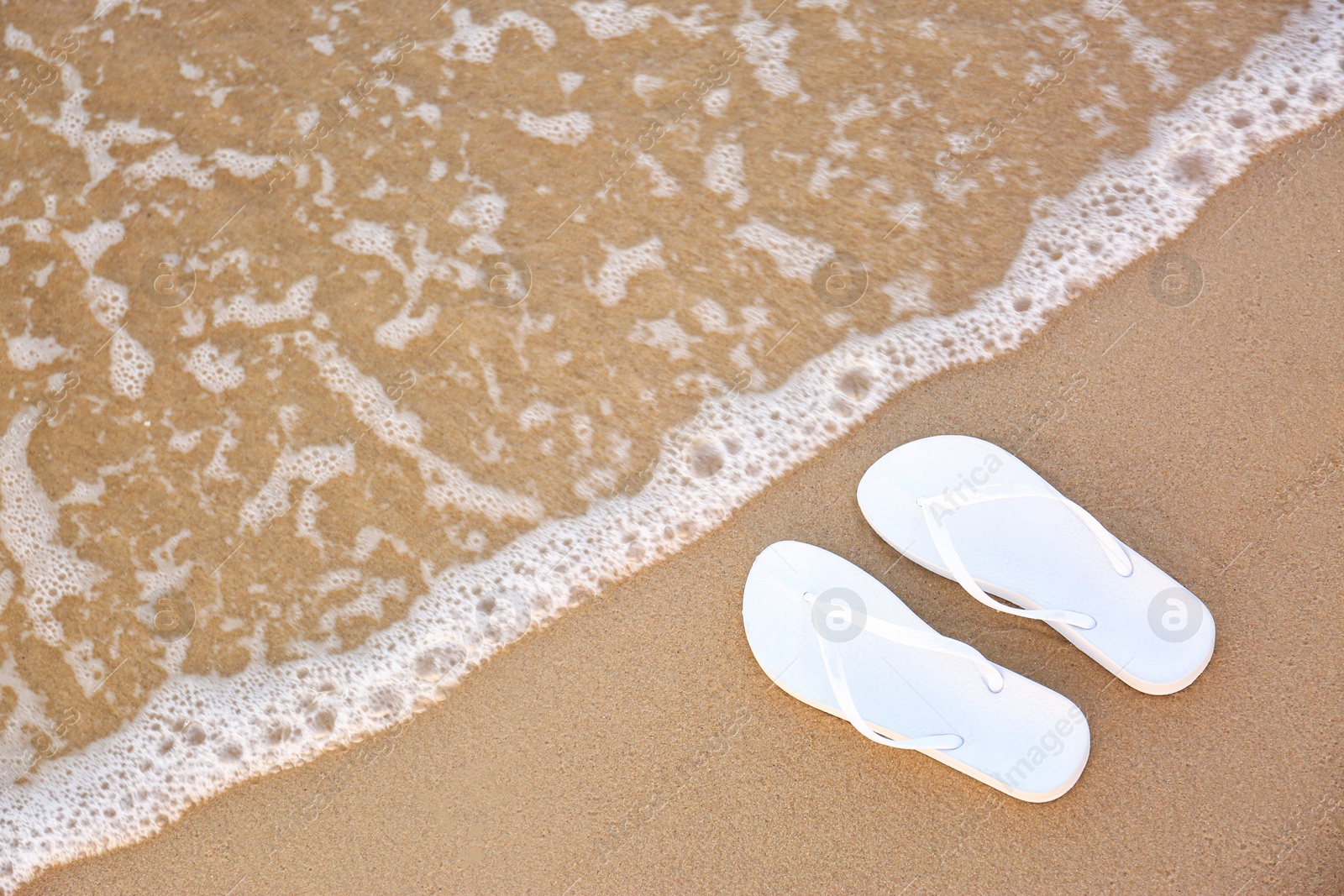 Photo of White flip flops on sand near sea, top view with space for text. Beach accessories