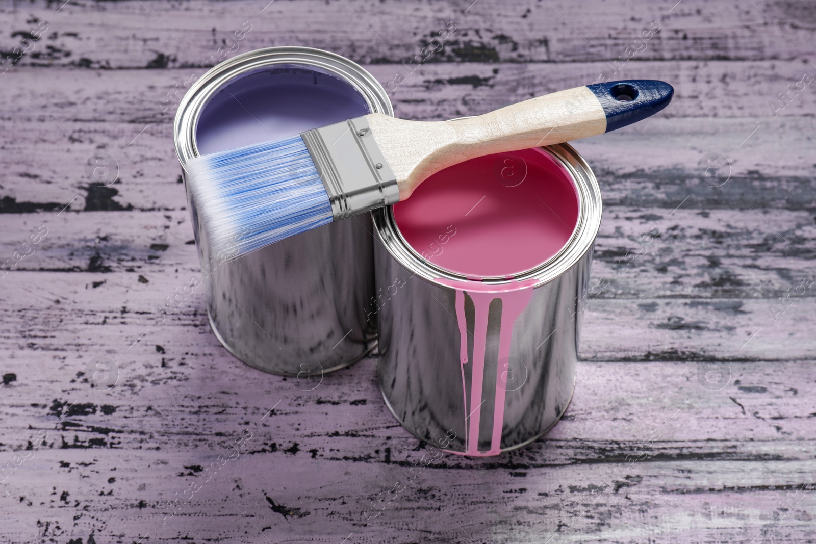 Photo of Cans of pink and lilac paints with brush on rustic wooden table