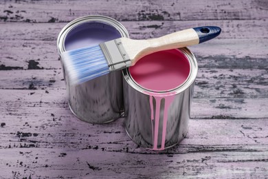 Cans of pink and lilac paints with brush on rustic wooden table
