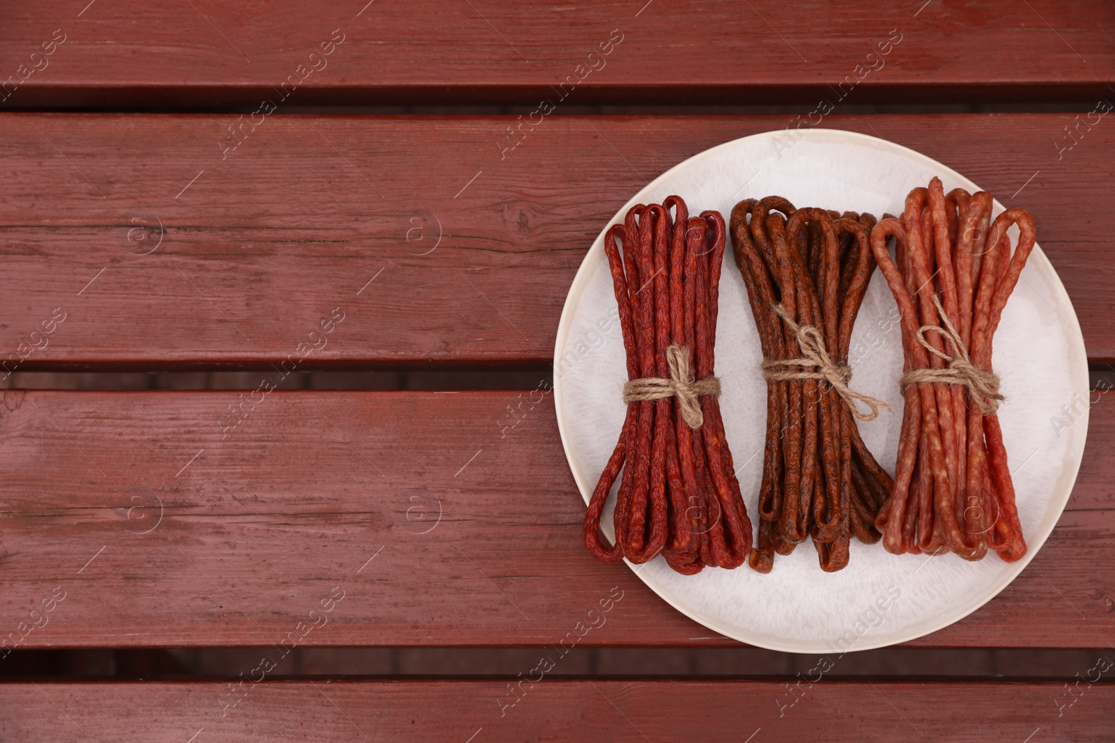 Photo of Bundles of delicious kabanosy on wooden table, top view. Space for text