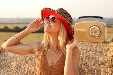 Happy hippie woman with receiver near hay bale in field