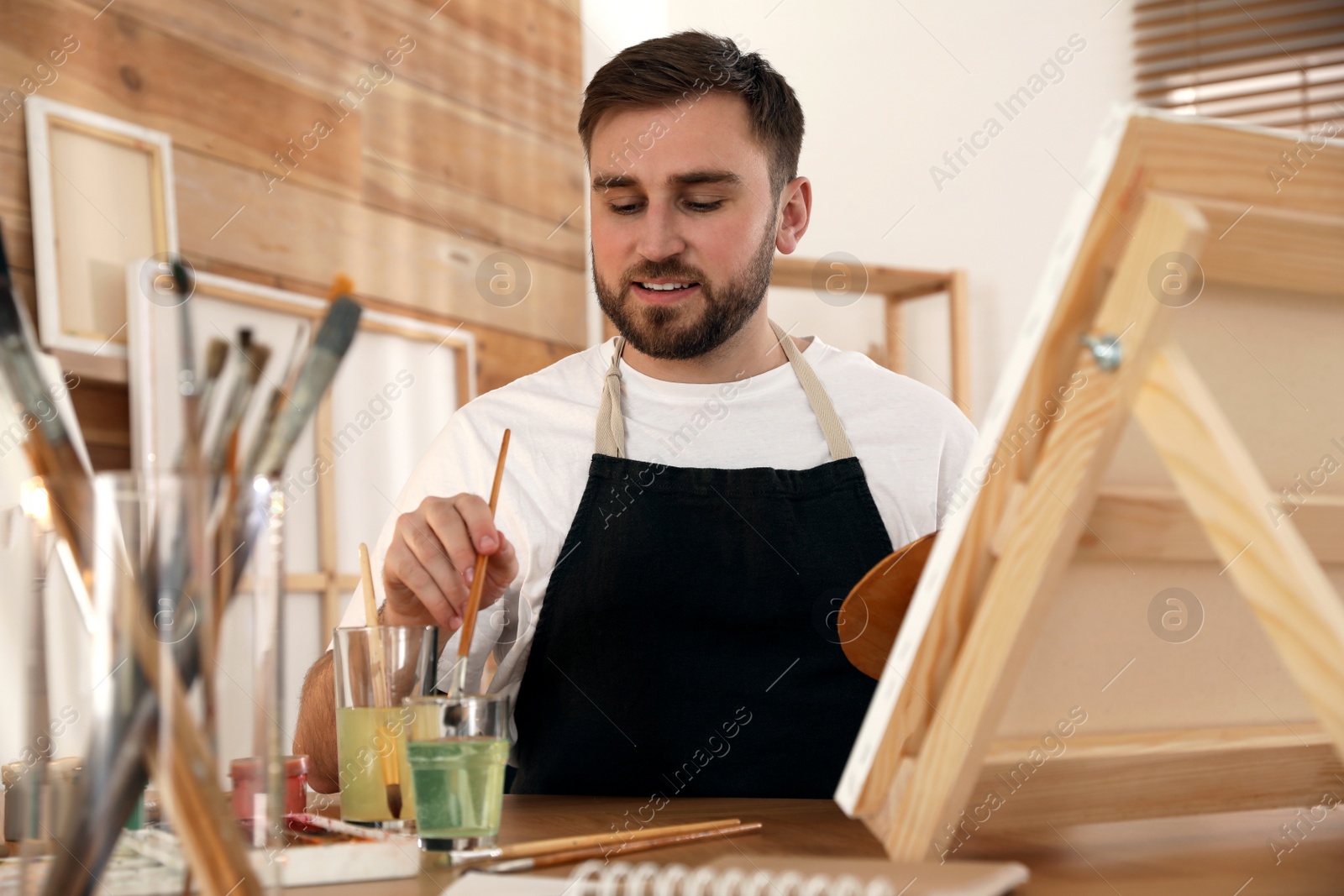 Photo of Young man painting on easel with brush in artist studio