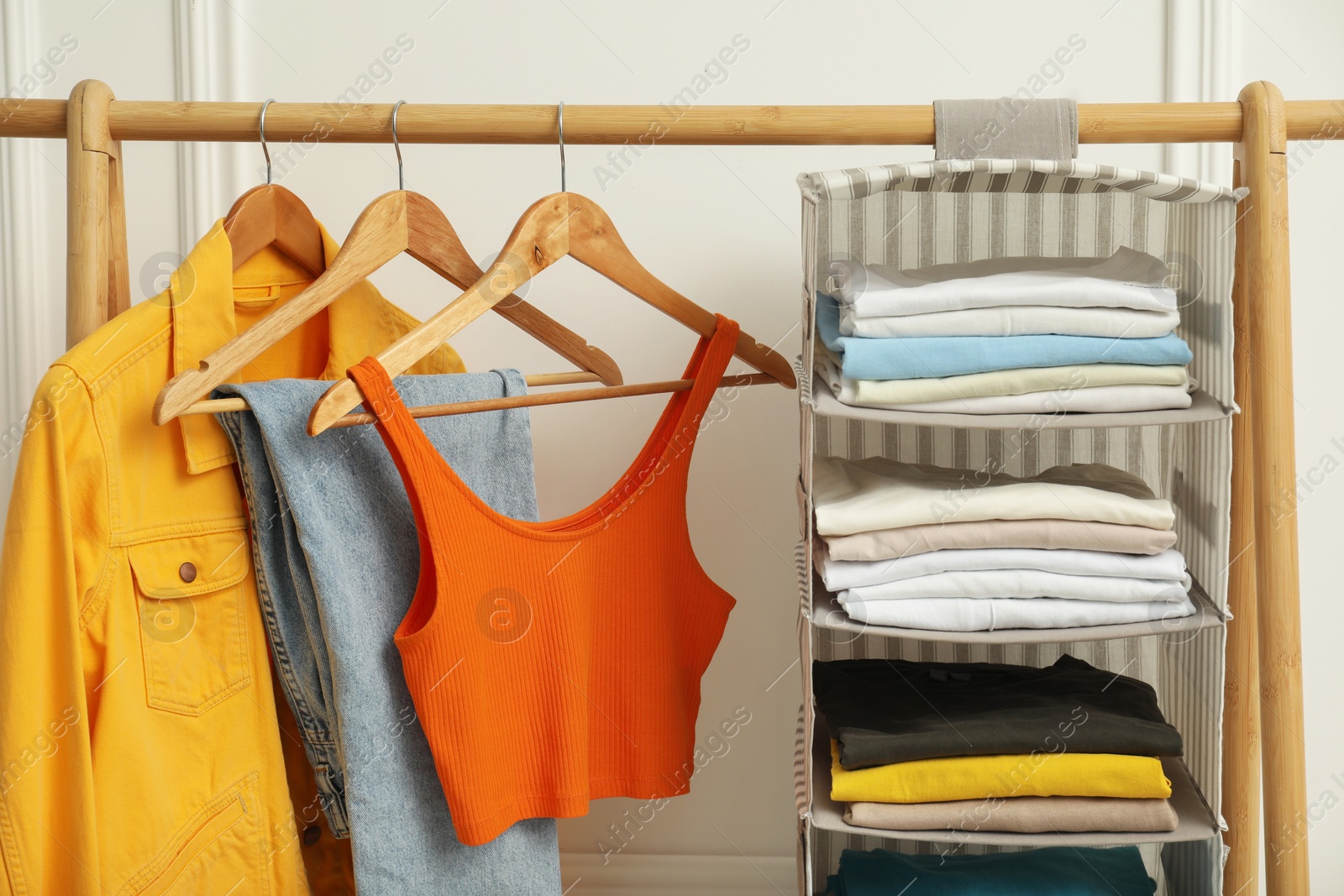 Photo of Wardrobe organization. Rack with different stylish clothes near white wall