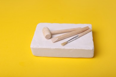 Photo of Educational toy for motor skills development. Excavation kit (plaster, digging tools and brush) on yellow background