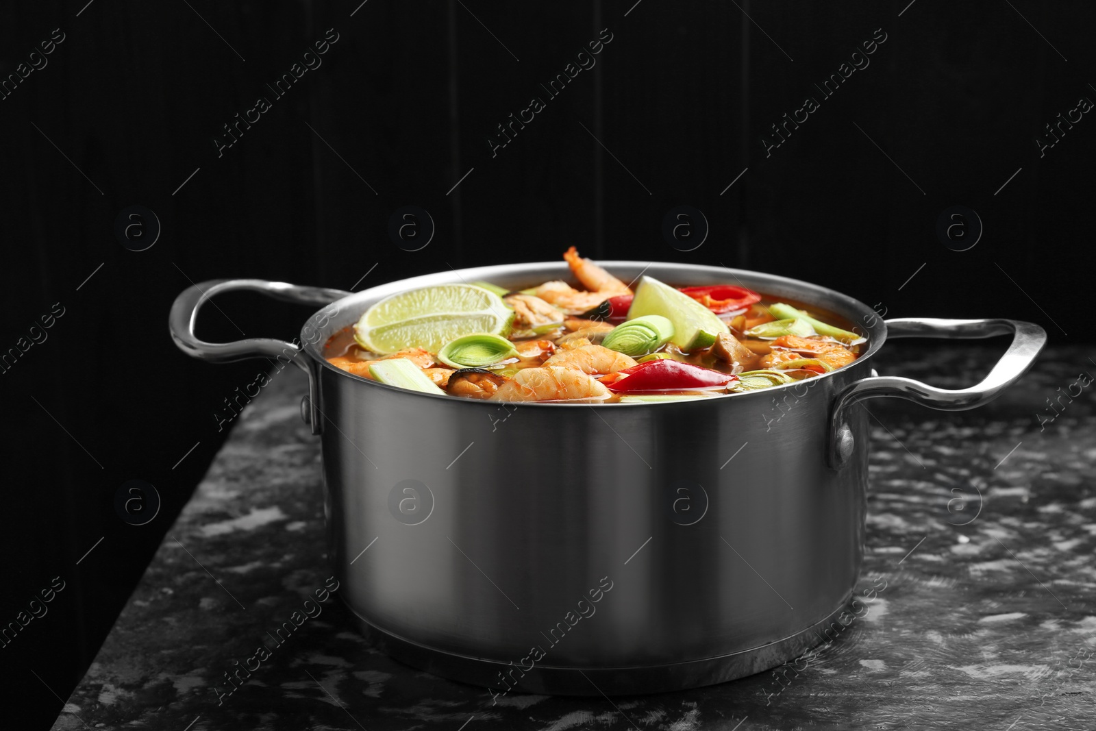 Photo of Saucepan with delicious Tom Yum soup on black marble table