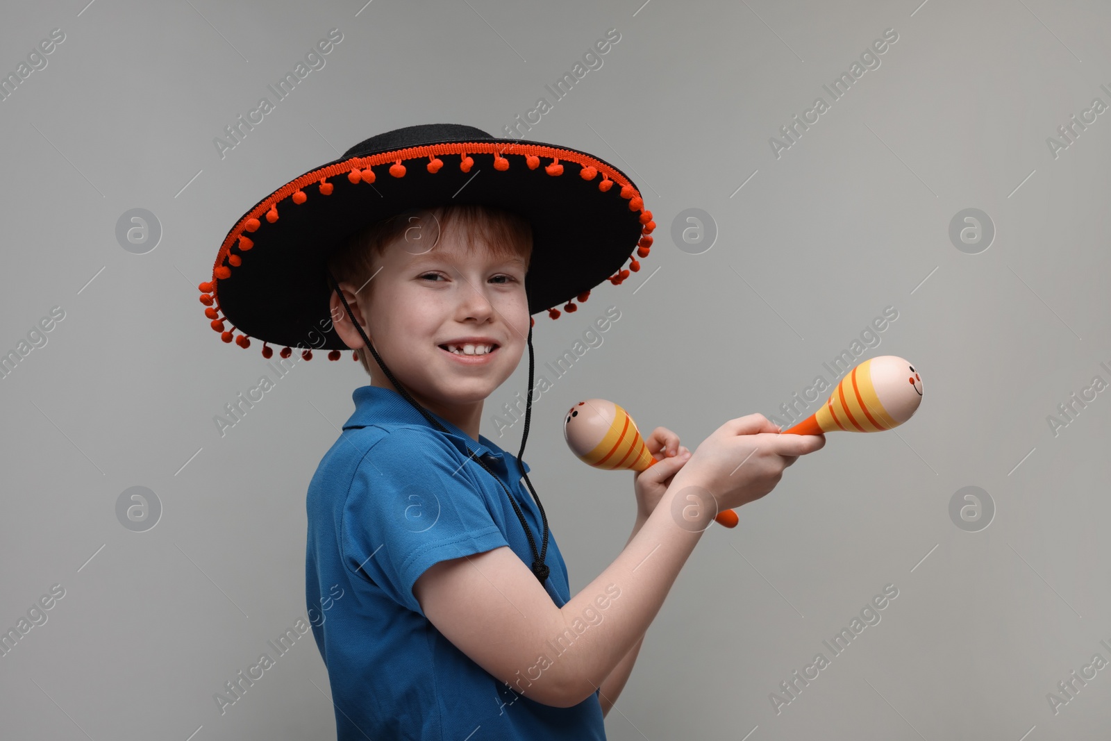 Photo of Cute boy in Mexican sombrero hat with maracas on grey background