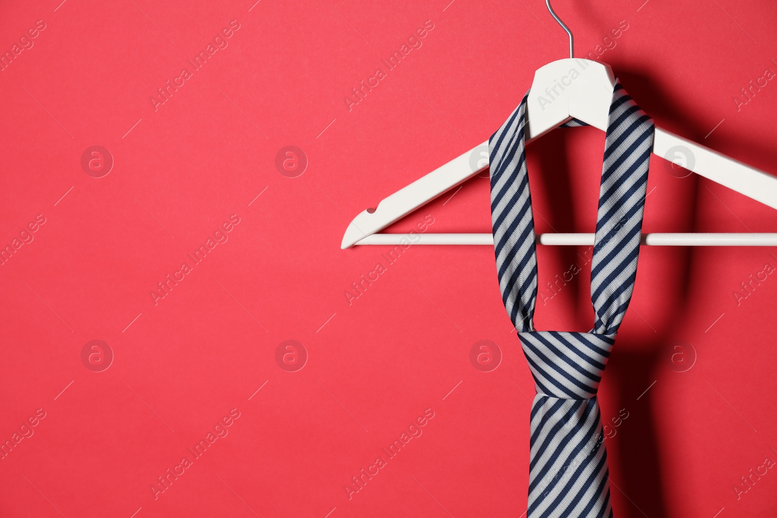 Photo of Hanger with striped tie on red background. Space for text