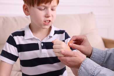 Photo of Woman putting sticking tape onto little boy`s hand on sofa, closeup