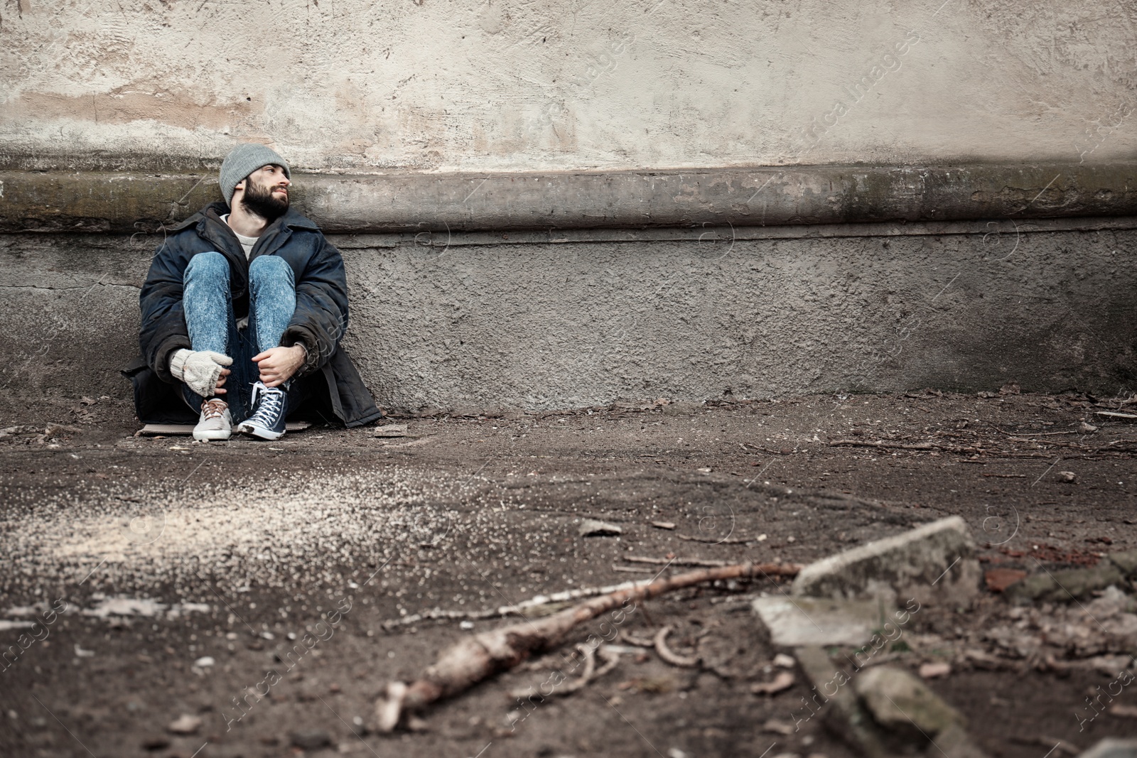 Photo of Poor homeless man sitting near wall on street. Space for text